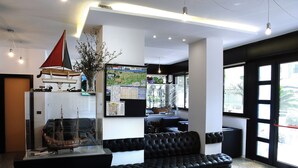 Ein modernes Wohnzimmer mit einem schwarzen Ledersofa, einem Modell eines Segelboots und einem großen Fenster mit Blick auf die Stadt.