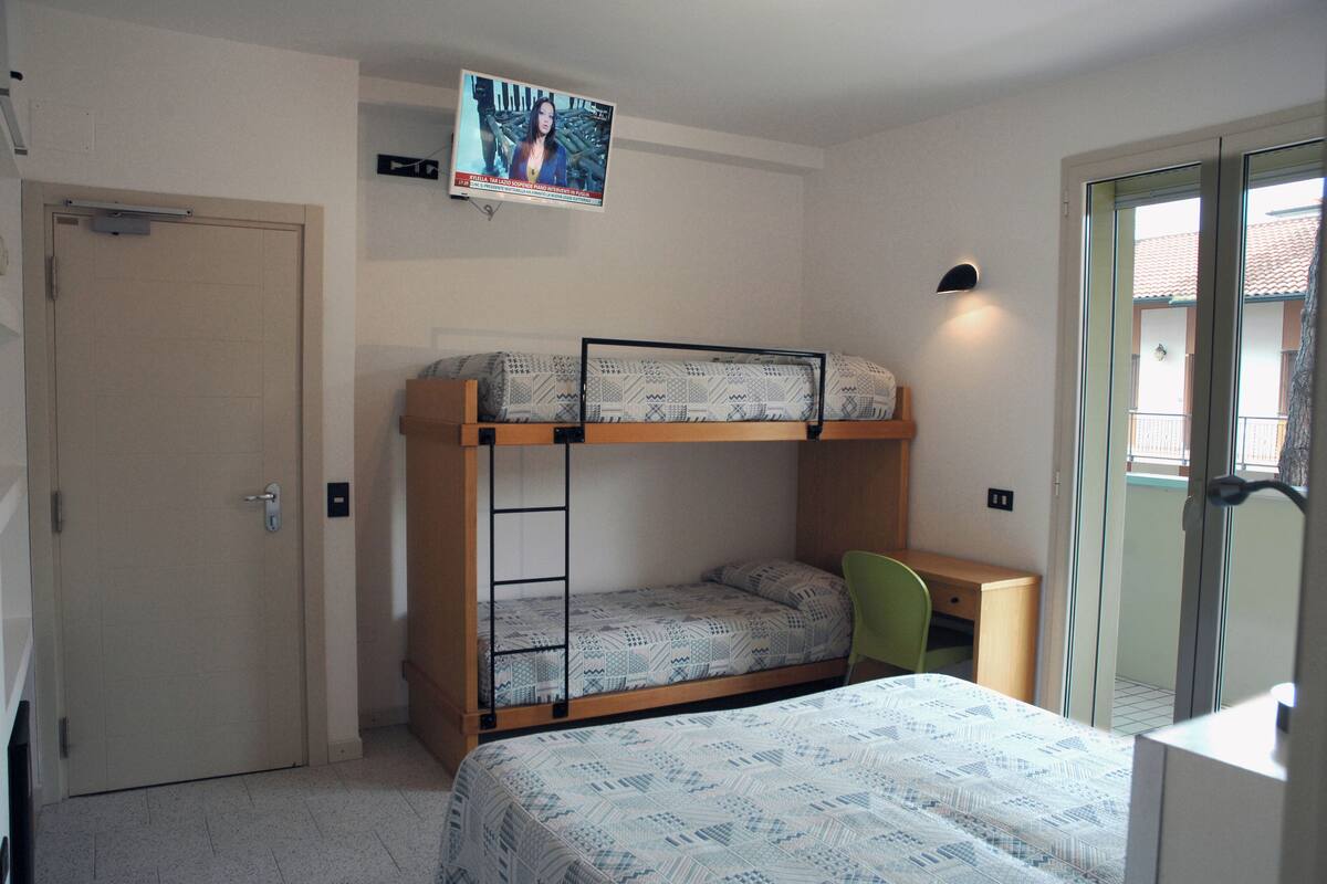 A compact hotel room with a bunk bed, a desk, a chair, and a television mounted on the wall.