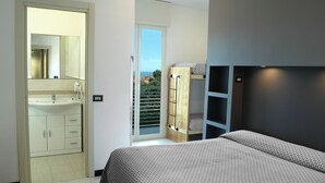 Ein Schlafzimmer mit Bett, Kleiderschrank, Badezimmer mit Waschbecken und einem Balkon mit Aussicht.