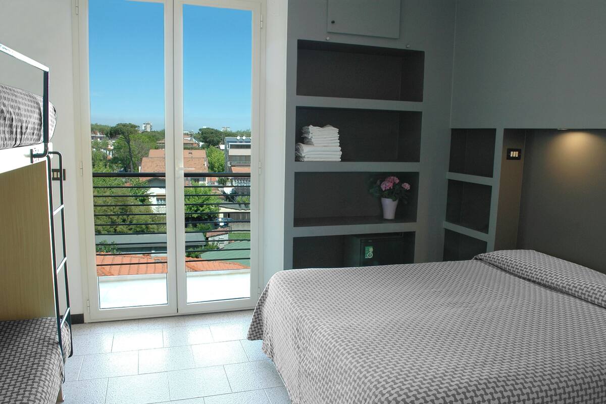 A bedroom with a bed, a wardrobe, a shelf with folded clothes, and a potted plant.