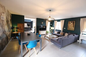 A modern living room with a grey sofa, blue chairs, a dining table, and a TV.