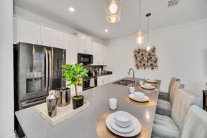 A modern kitchen with stainless steel appliances, a central island, and a dining area with a sofa. - Disney Near: 4BR Resort Oasis w/ Pool & Theme Room (Kissimmee)