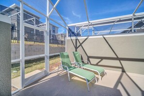 Ein überdachter Außenbereich mit zwei grünen Liegestühlen, Blick auf ein Gebäude im Hintergrund und einem Metallzaun.