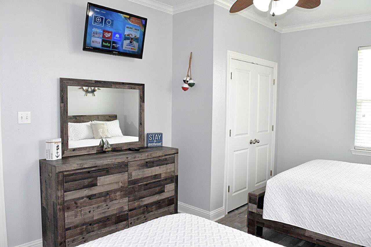A bedroom with a wooden dresser, a bed, a television mounted on the wall, and a white door.