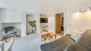 A modern living room with a grey sofa, a wooden coffee table, a grey armchair, a TV mounted on the wall, and a potted plant. - Lovely Apartment - Central Oxford - Pass the Keys (Oxford)