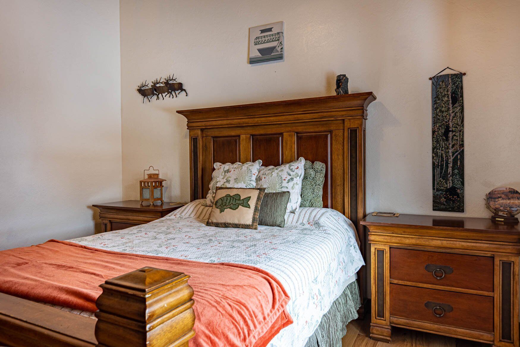 A bedroom with a wooden bed, a nightstand, a dresser, and a wall-mounted tapestry.