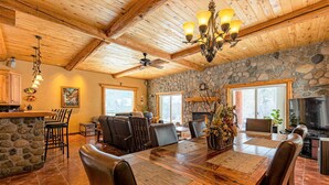 A spacious dining area with a stone accent wall, a wooden ceiling, and a chandelier. - Riverfront | Close to Skiing, New Hot Tub! (Pagosa Springs)