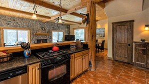 A rustic kitchen with stone walls, wooden beams, and a stone fireplace. - Riverfront | Close to Skiing, New Hot Tub! (Pagosa Springs)