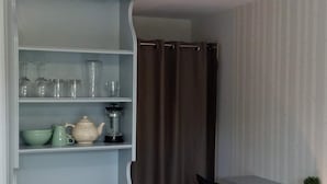 Una habitación con un armario blanco de puertas de cristal, una silla negra, una mesita y una cortina.