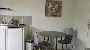 Cocina compacta con refrigerador, lavamanos y comedor con dos sillas y una mesa.
