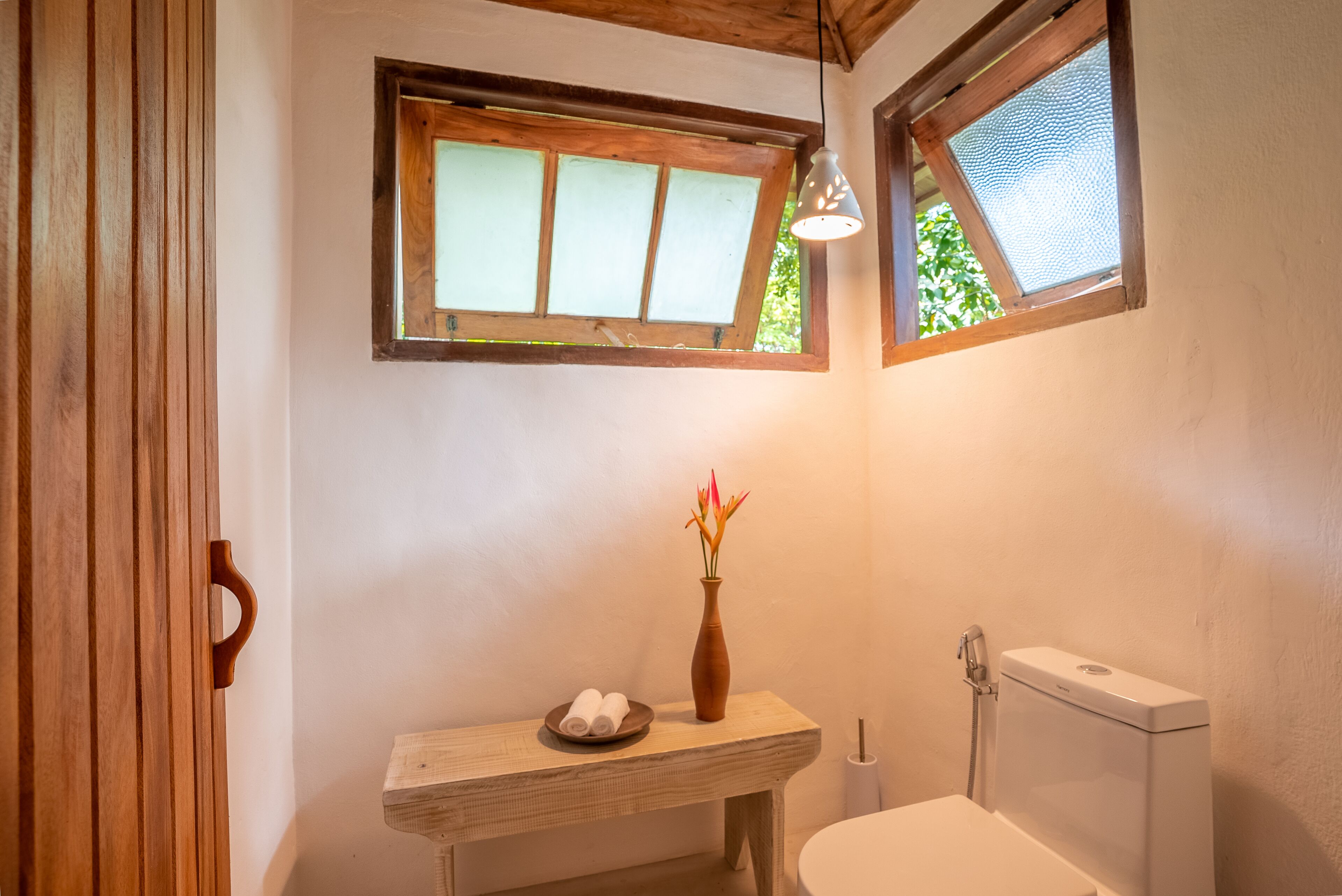 Une salle de bain avec un meuble-lavabo en bois, un vase avec des fleurs et des toilettes.