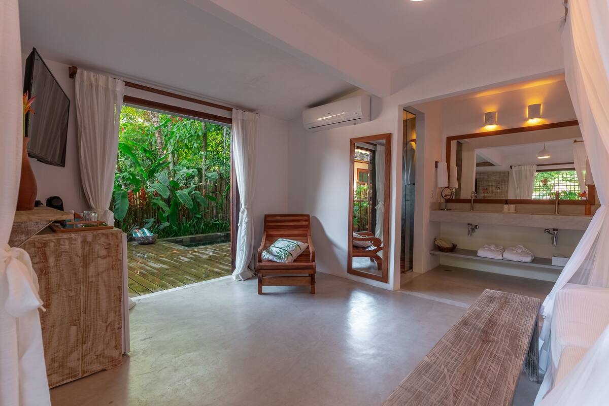 Una habitación con una cama de madera, una mesita, un espejo y vistas a un jardín exuberante.
