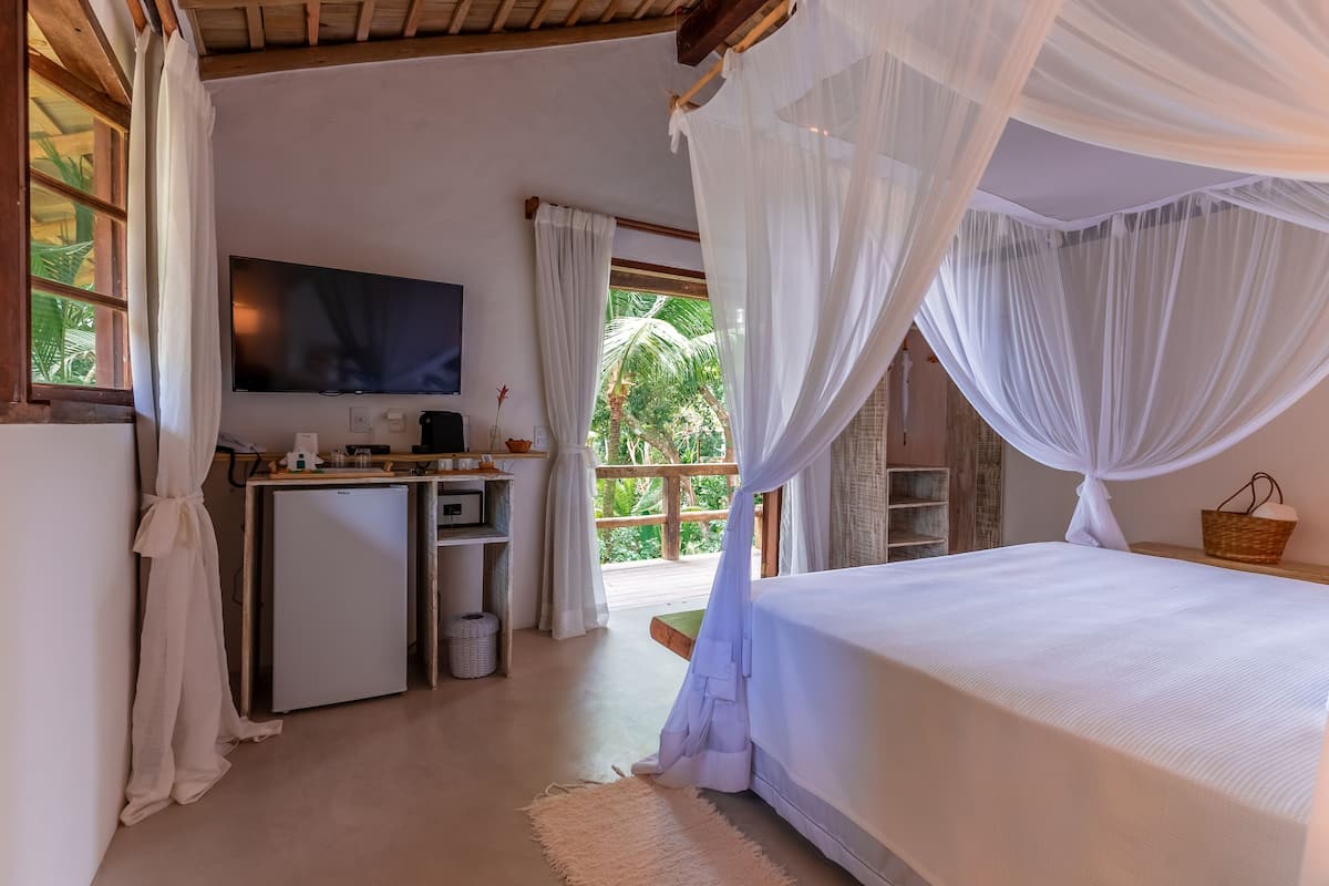 Un dormitorio con cama, escritorio, televisor y balcón con vistas a zonas verdes.