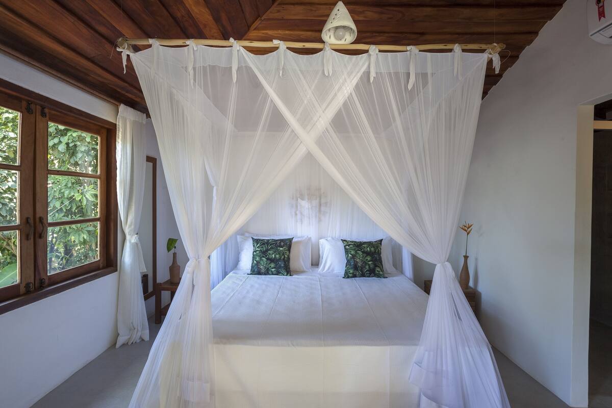 Un dormitorio con cama con dosel, techo de madera y ventana con cortinas.