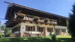 Ein zweistöckiges Gebäude mit Balkon, Holzläden und Außenbestuhlung.