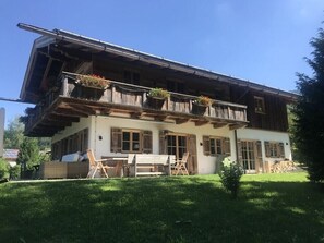 A two-story building with a balcony, wooden shutters, and outdoor seating.