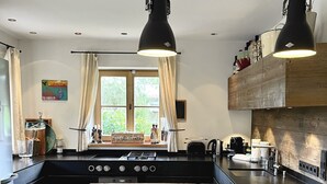 Eine moderne Küche mit einer zentralen Kochinsel, Pendelleuchten und Blick ins Freie durch große Fenster.