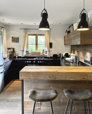 A modern kitchen with a central island, pendant lighting, and a view of the outdoors through large windows.