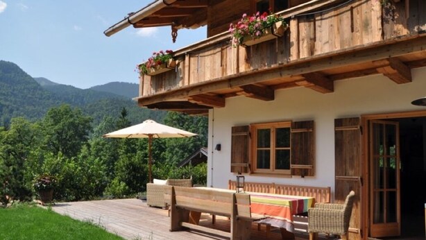 Eine Holzhütte mit Balkon, Bank und Tisch vor der Tür.