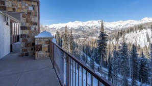 Un bâtiment en pierre doté d’un balcon qui offre une vue sur des montagnes enneigées et une forêt.
