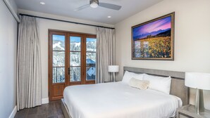 Une chambre d’hôtel avec un grand lit, un ventilateur de plafond, un tableau représentant un paysage de montagne et une vue sur des montagnes enneigées par la fenêtre.