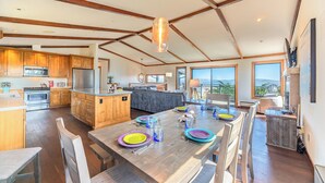 Une cuisine spacieuse avec des meubles en bois et un îlot central, un coin repas agrémenté d’assiettes colorées, et de grandes fenêtres offrant une vue sur l’extérieur.