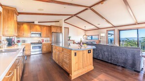 Een ruime keuken met houten kastjes, een centraal eiland en een groot raam met uitzicht op de omgeving.