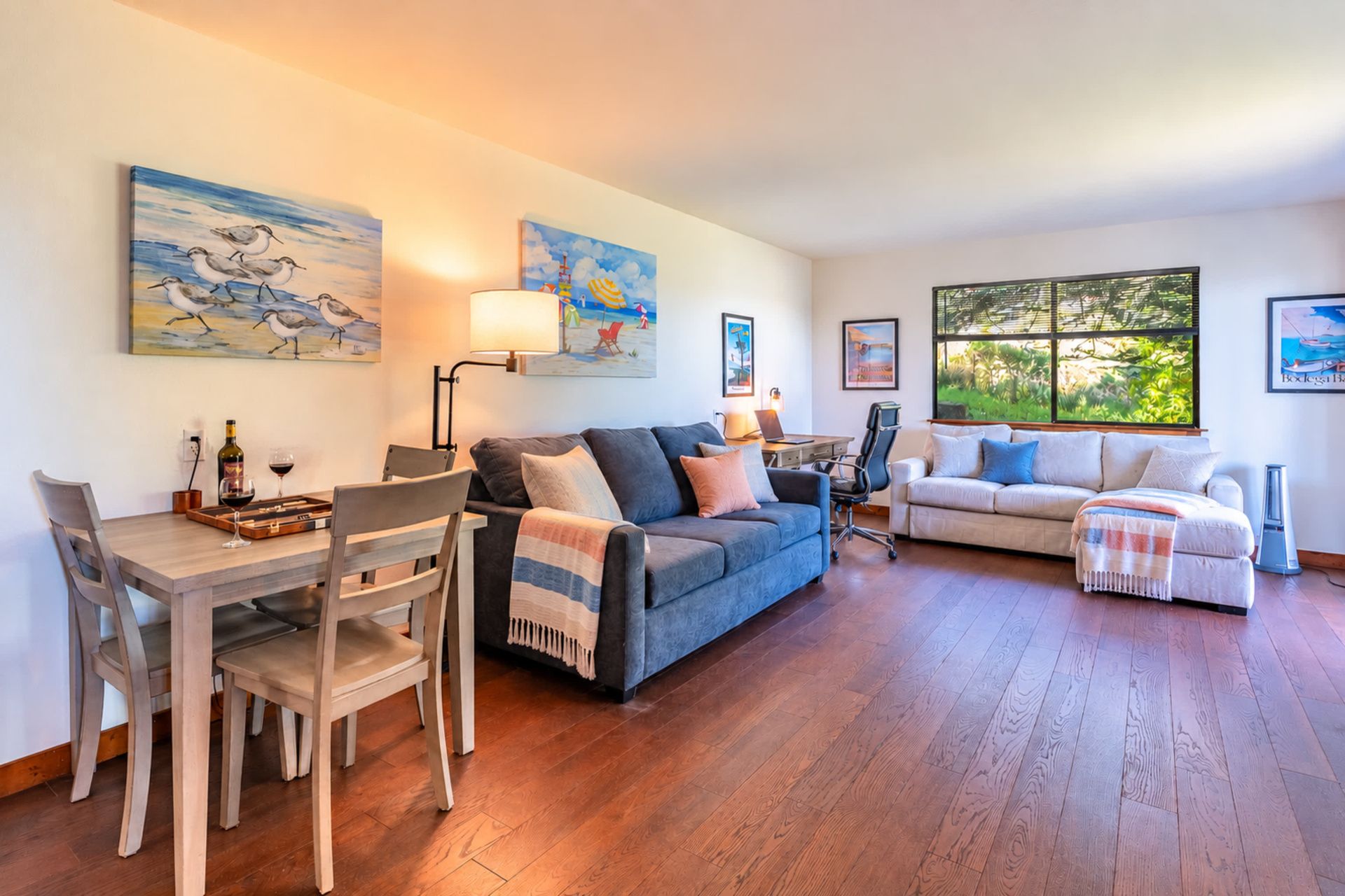 A living room with a dining area, two sofas, a coffee table, and artwork on the walls.
