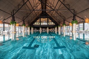 Una amplia piscina cubierta con techos altos y diseño moderno, rodeada de zonas de estar y grandes ventanales.