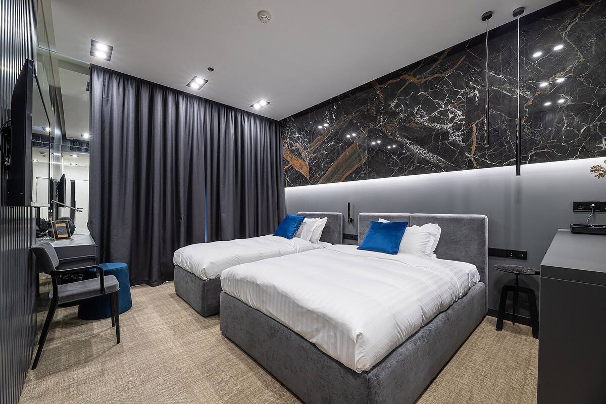 Quarto de hotel moderno com duas camas, uma escrivaninha e uma grande parede de mármore.