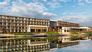 A modern hotel with multiple floors, large windows, and a reflection in the water. - Emily Resort (Lviv)