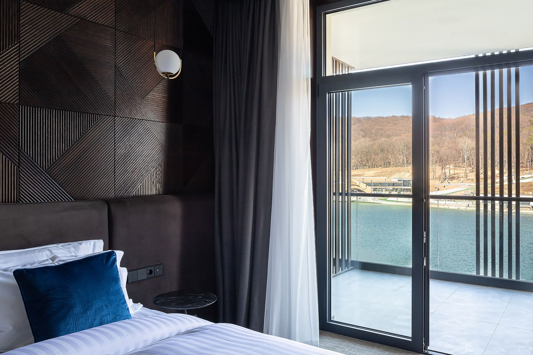 A modern hotel room with a large window overlooking a body of water and hills.