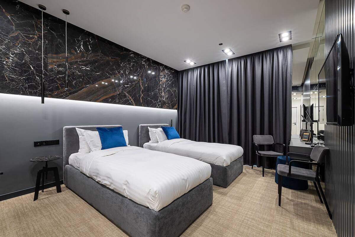Quarto de hotel moderno com duas camas, uma escrivaninha e um espelho grande.