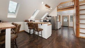 A modern kitchen with a central island, wooden bar stools, and a lofted seating area.