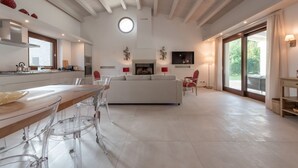 Un vaste espace de vie comprenant un grand canapé blanc, une table à manger avec des chaises, un coin cuisine et une grande fenêtre laissant entrer la lumière naturelle.