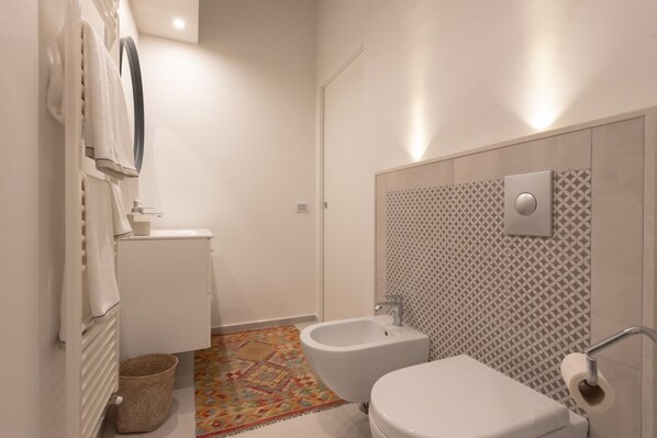 Ein modernes Badezimmer mit Toilette, Bidet und einer Wand mit Musterfliesen in der Dusche.