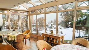 Una habitación luminosa con ventanas amplias, muebles de mimbre y una vista nevada al exterior.