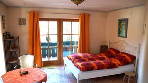 Un dormitorio con una cama, una silla, una mesa y un ventanal con cortinas.