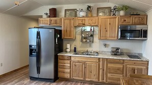 A modern kitchen with wooden cabinets, a stainless steel refrigerator, a microwave, and a granite countertop.