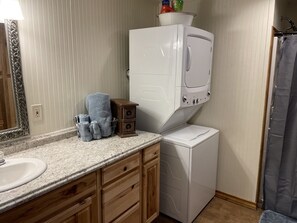 A compact bathroom with a sink, a mirror, a white washing machine, and a small cabinet with towels. - Cozy Cabin (Tuscola)