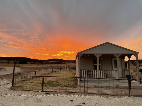 A small, single-story building with a porch, surrounded by a gravel area and a metal fence. - Cozy Cabin (Tuscola)