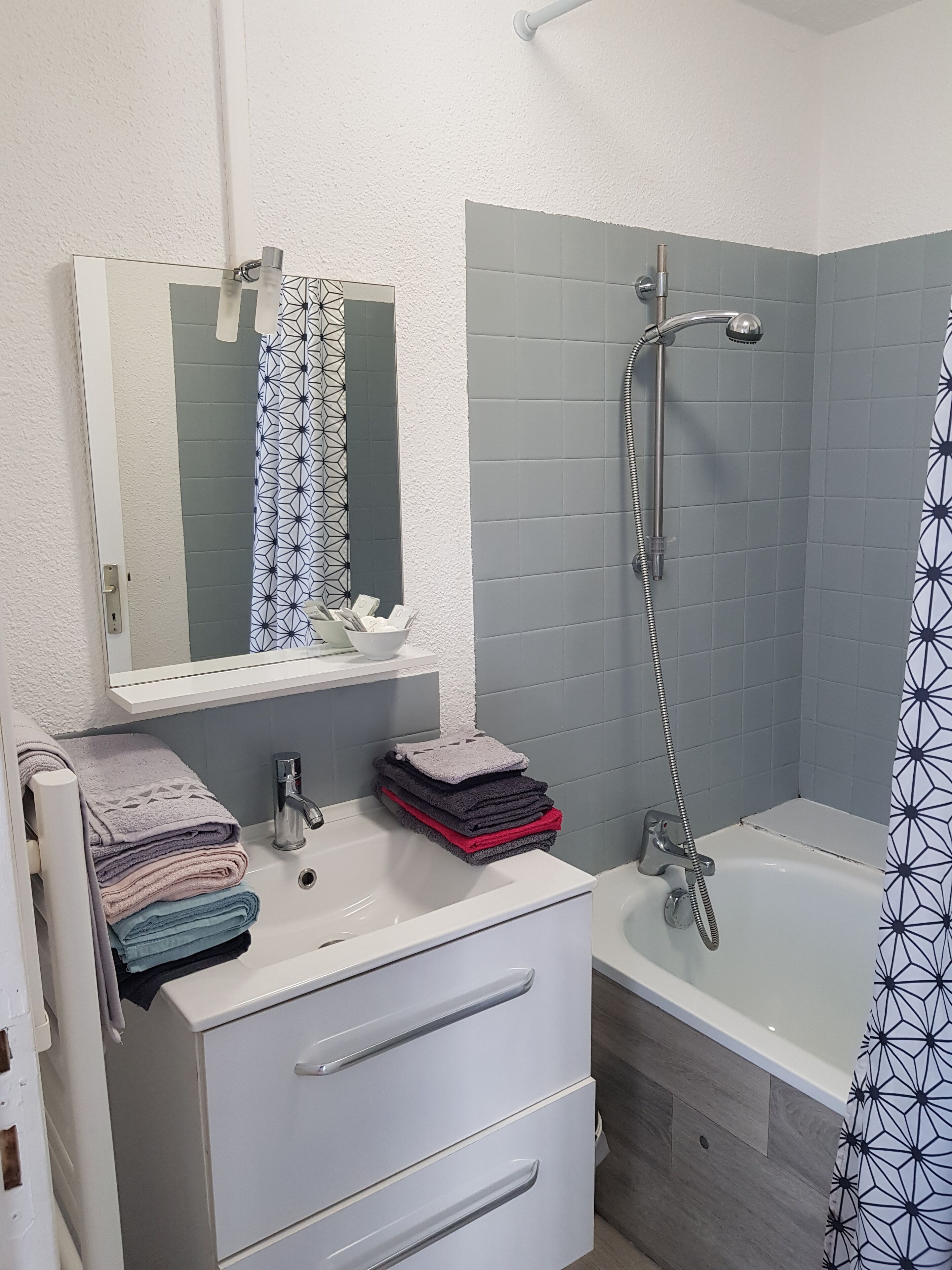 Une salle de bain avec un meuble-lavabo blanc, un miroir, un évier, une pile de serviettes, une douche avec un pommeau de douche à main et une baignoire.