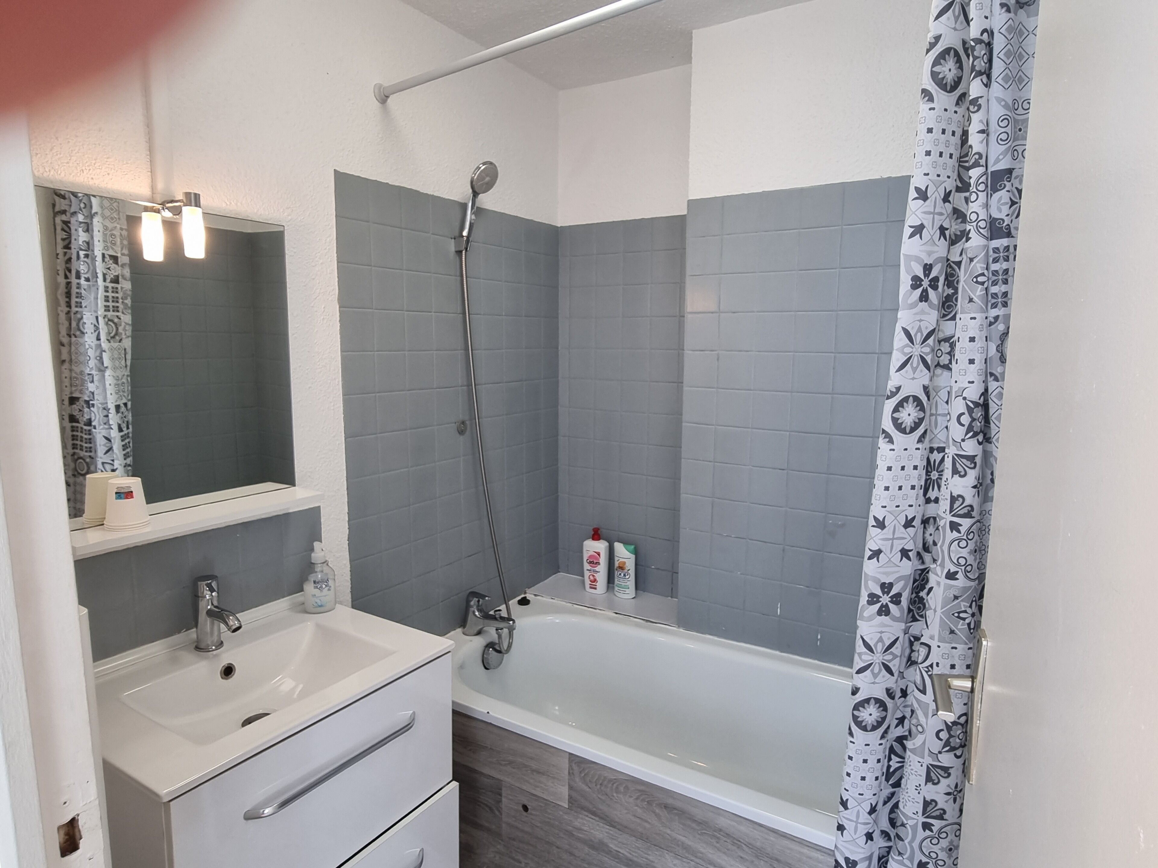 Ein Badezimmer mit einem weißen Waschbecken, einem Spiegel, einer Dusche mit Regendusche und einer Badewanne.