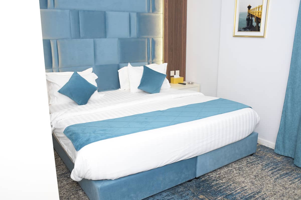 A neatly made bed with blue and white bedding, a tufted headboard, a bedside table with a lamp, and a framed picture on the wall.