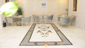 A lobby with a central decorative floor pattern, seating arrangements, and wall-mounted light fixtures. - Areen Hotel Airport (Jeddah)