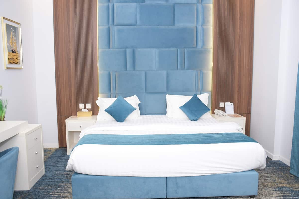 A hotel room with a large bed, a wooden headboard, a bedside table, and a nightstand.