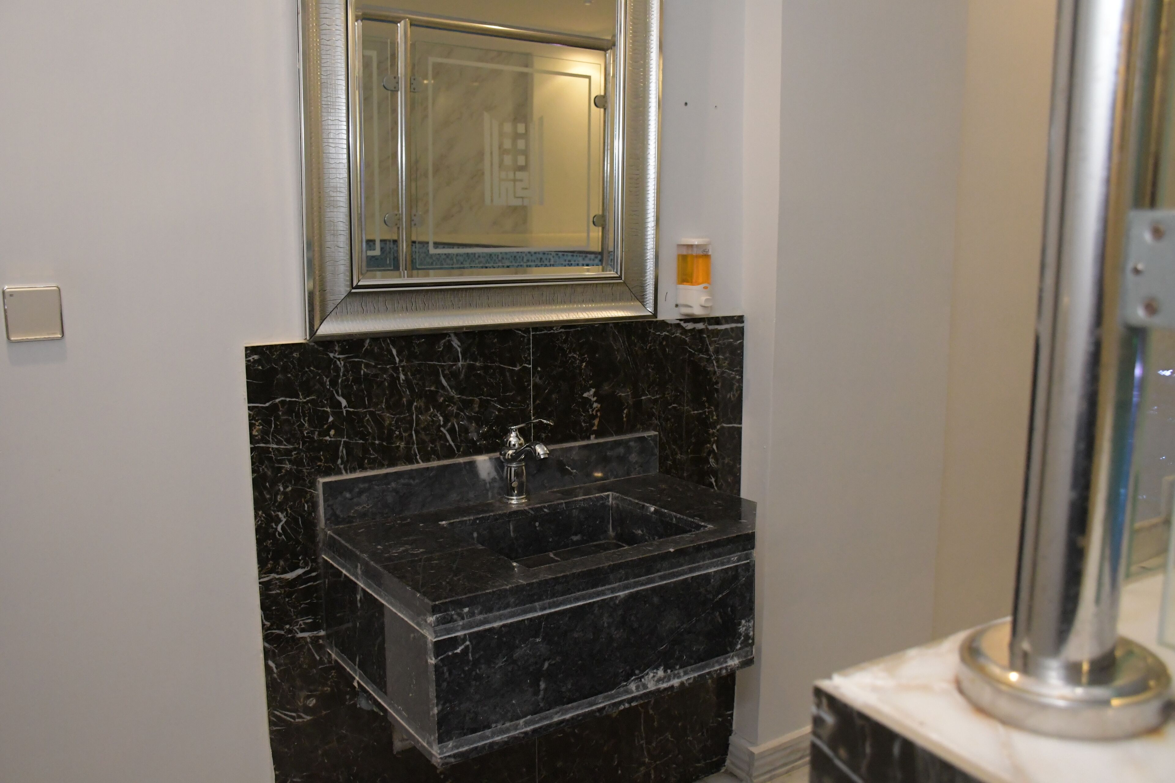 Un baño con lavamanos de mármol negro, un espejo y una ducha.