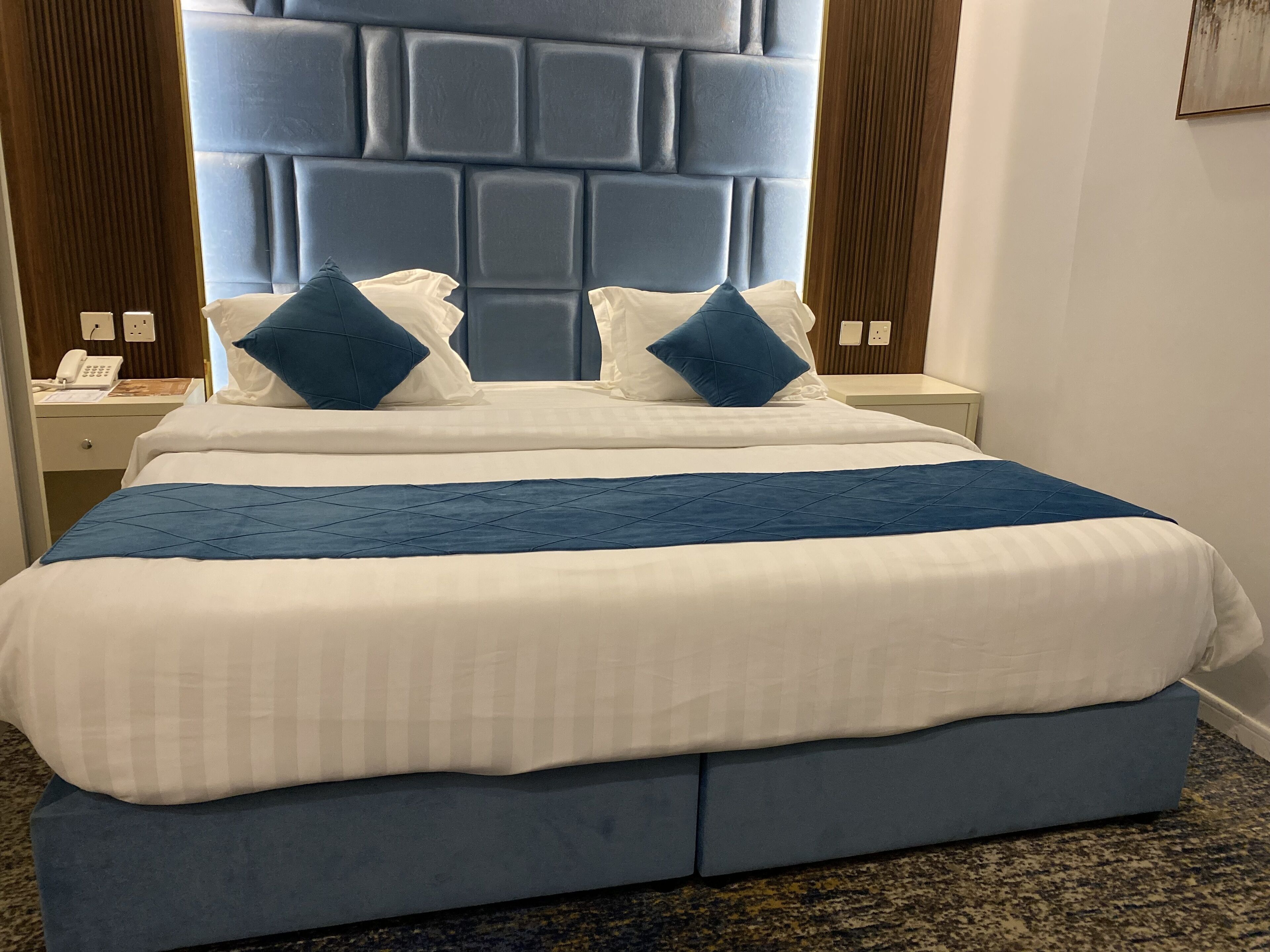 A hotel room with a large bed, two nightstands, a telephone, and a wall-mounted light switch.