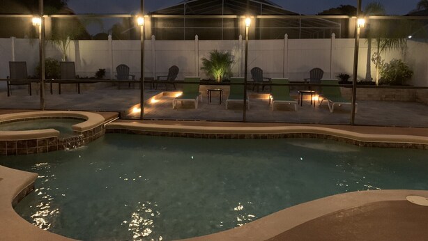Area piscina con lettini e vasca idromassaggio, circondata da una struttura coperta illuminata.