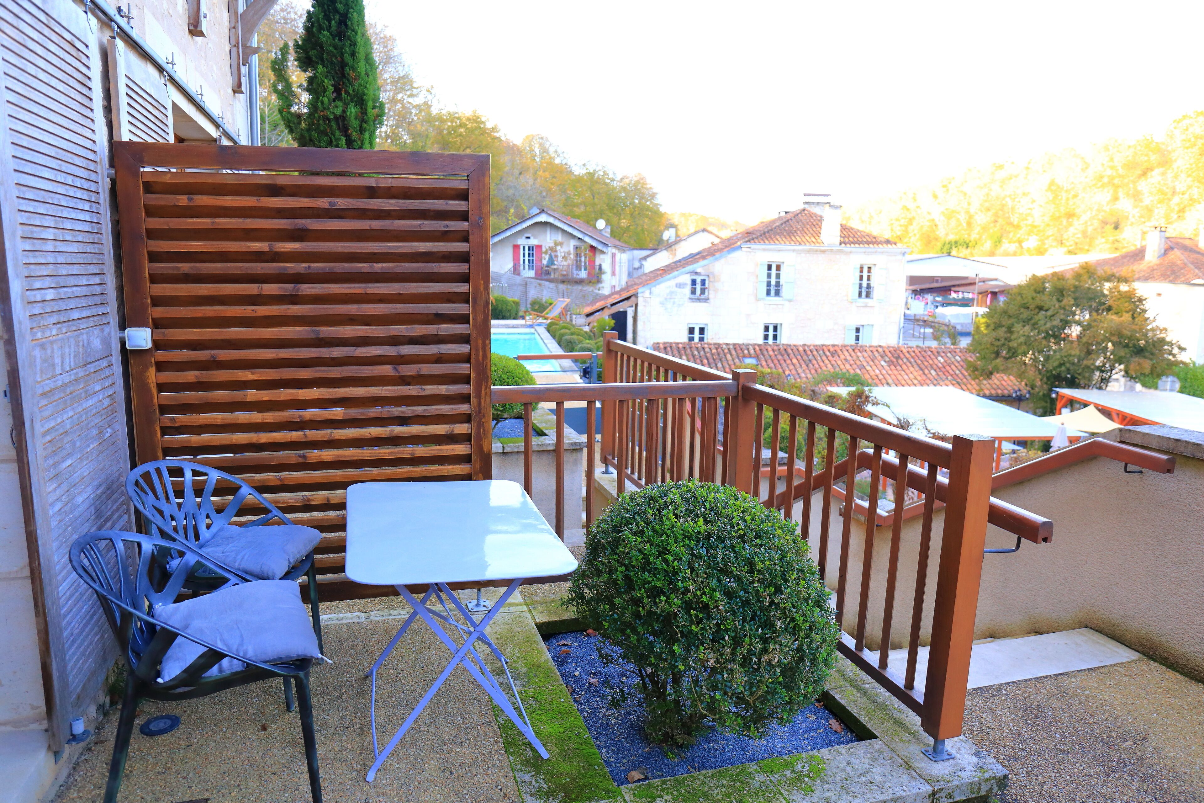 A balcony with a wooden fence, a small table, two chairs, and a potted plant.